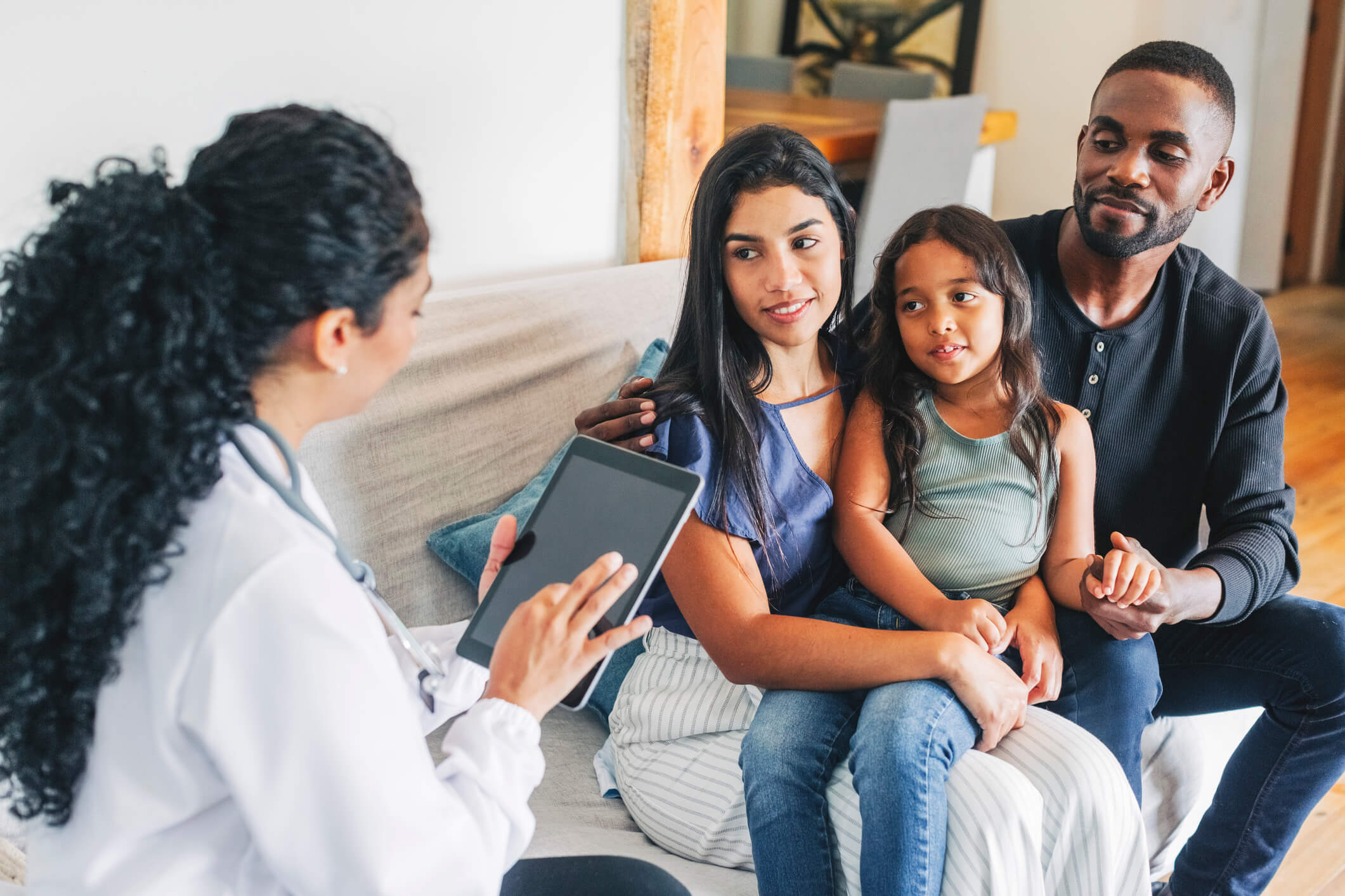 A young family sitting down across from a doctor who is noting something on her tablet.