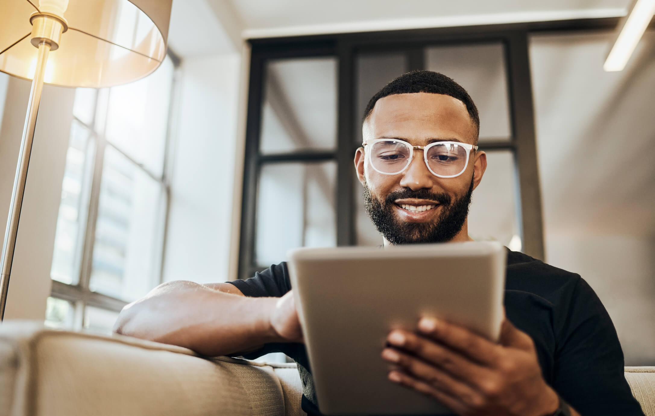 Young man wearing glasses sitting down and looking at a tablet.