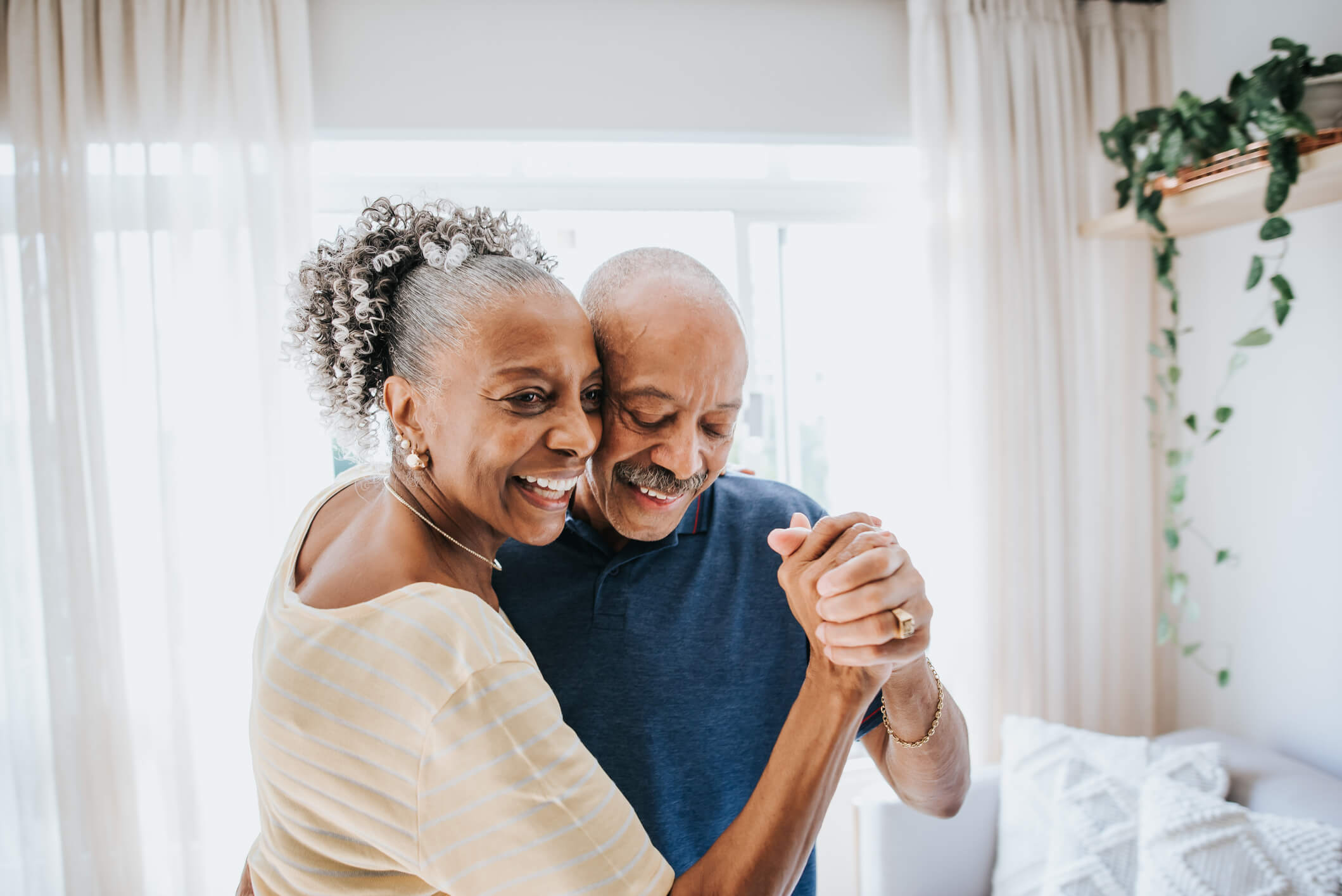 An older couple dancing and laughing in their living room.