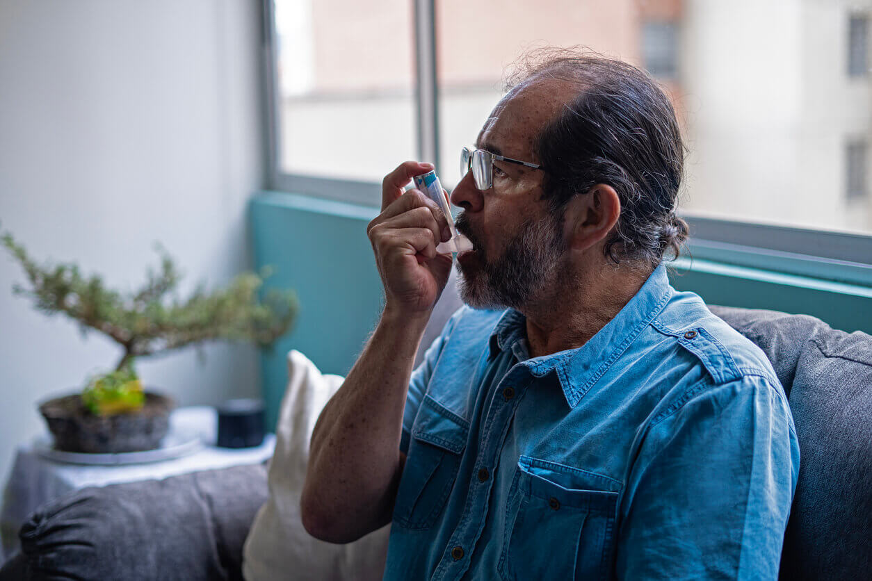 An older male asthma sufferer using an inhaler at home.