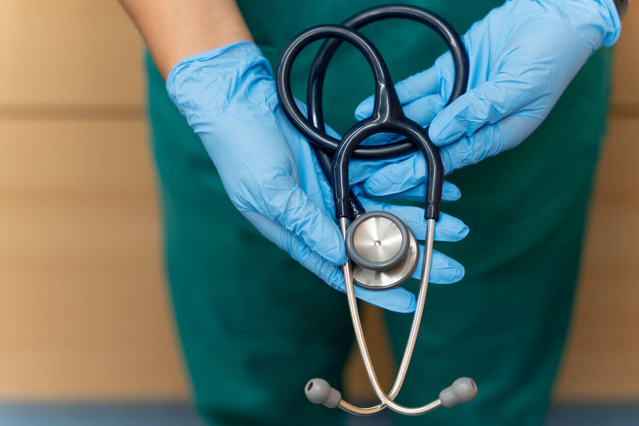 Hands with blue gloves of a doctor holding a stethoscope.