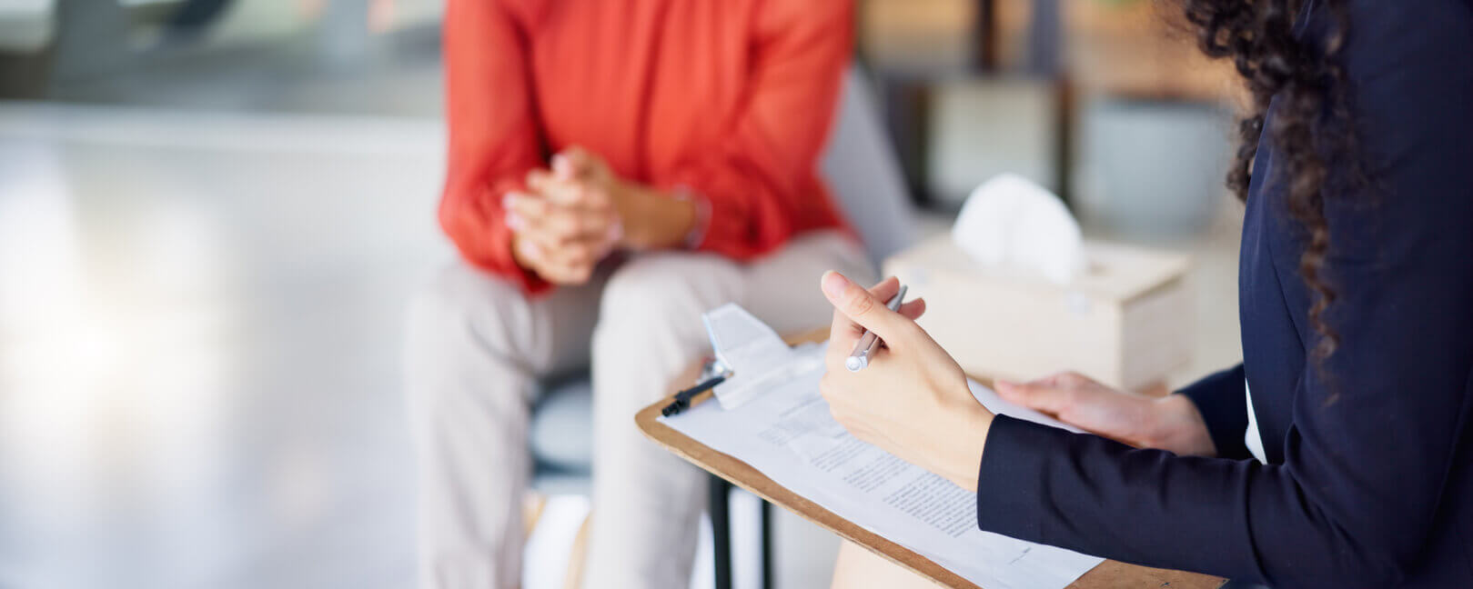 Therapist with clipboard is consulting client through talk therapy services.